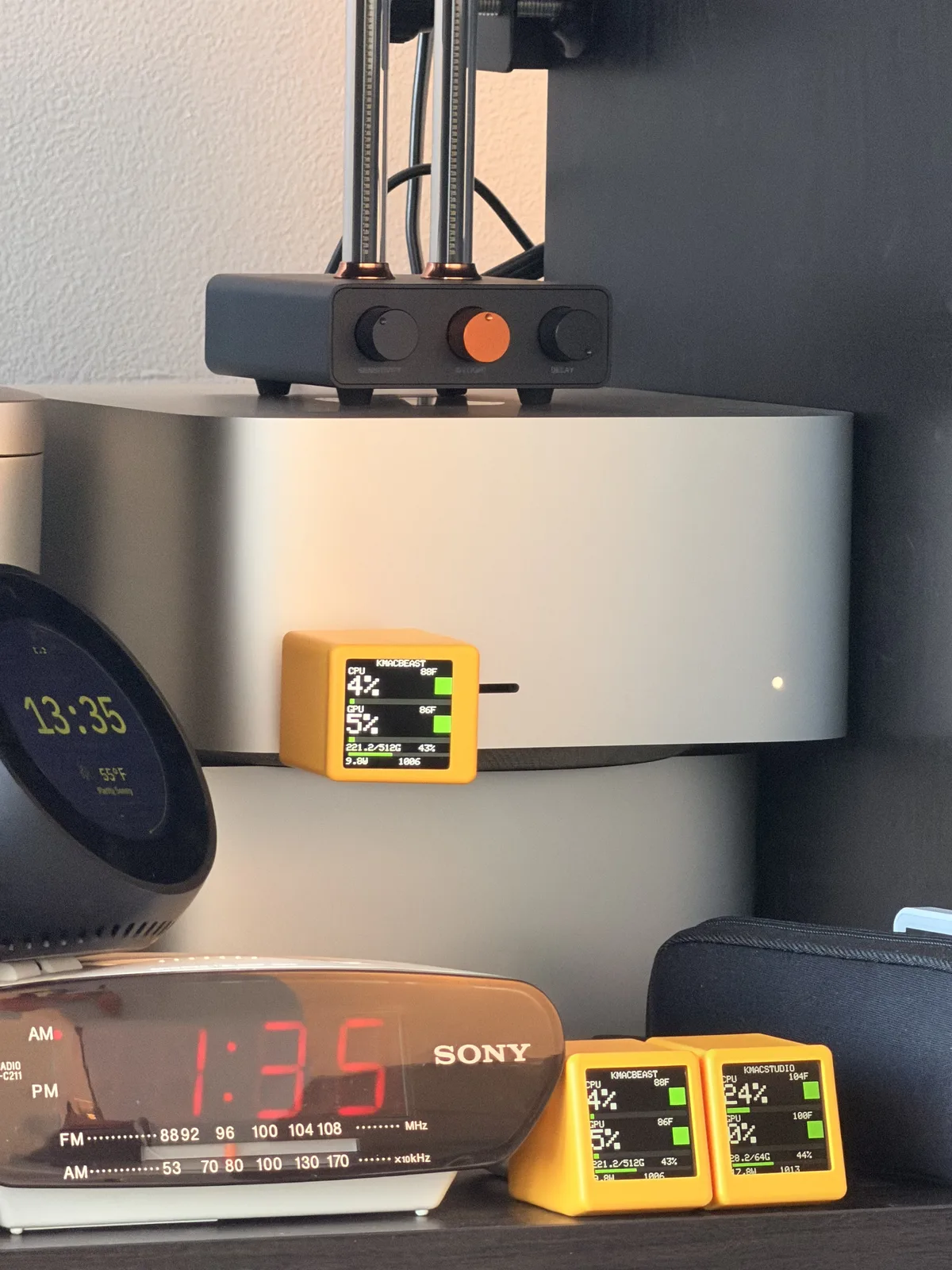 A shelf with a Mac Studio, a smart clock, a Sony clock radio, and three orange SmallTV cubes, one plugged into the Mac and two on the shelf below